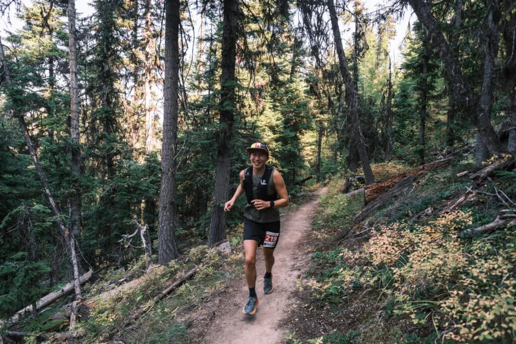 A smiling Golden Six Hour runner wearing a gold hat on a forest trail