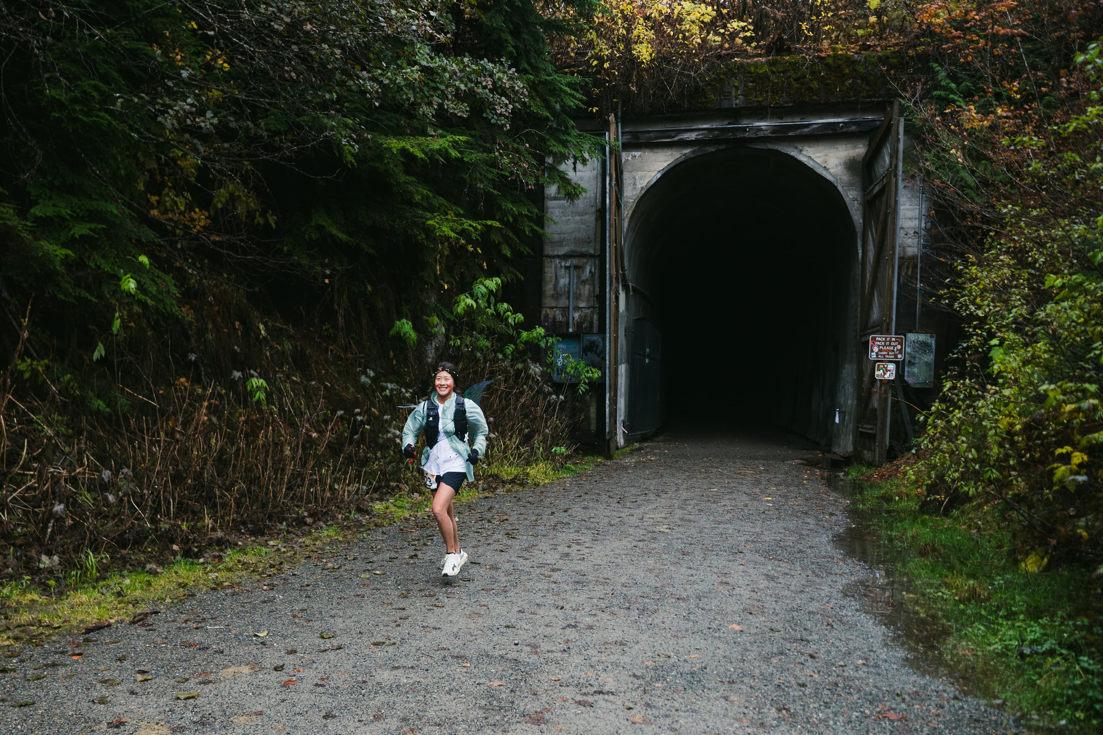 A smiling Hyak Passage runner passing the forested tunnel entrance