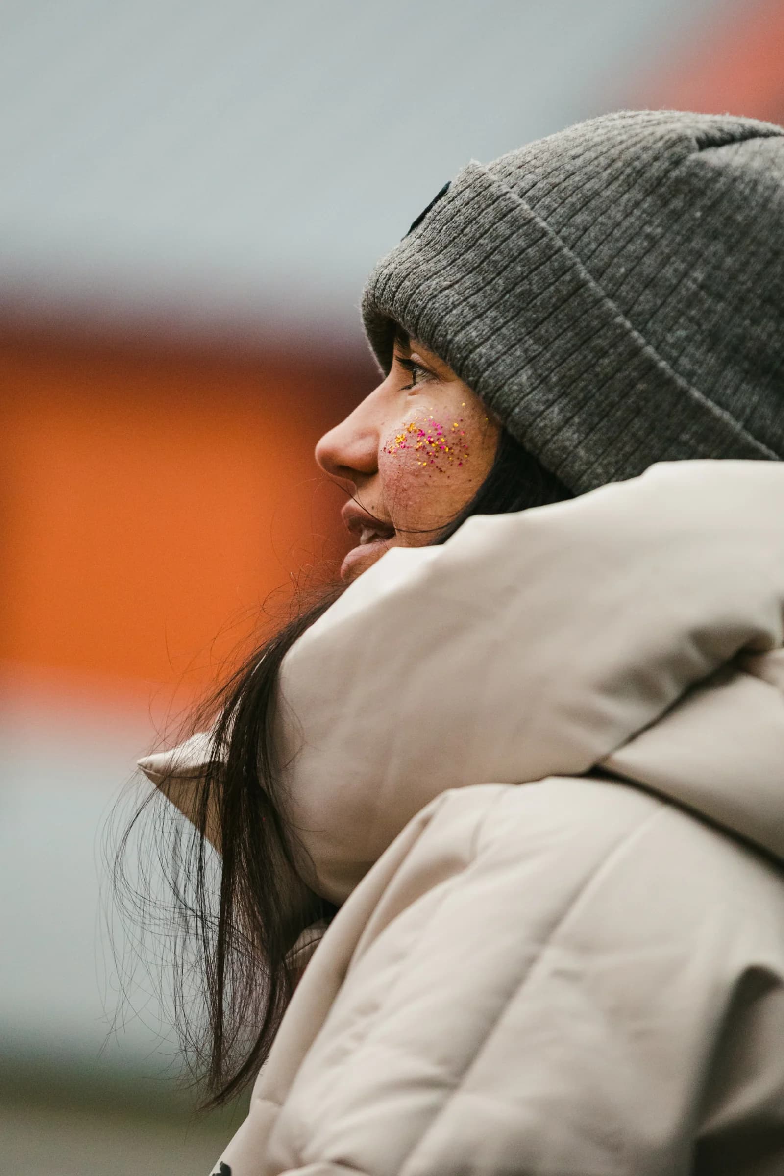 A person in a knit beanie with colorful glitter on their cheek